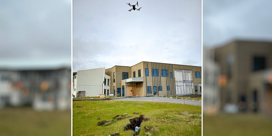 Eine Drohne fliegt in der Luft und hält ein Messystem an einem Seil über den Boden.