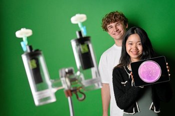 Two young people in portrait against a green background. Next to them is a sketch of a fuel cell.