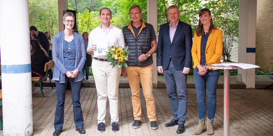 Group photo with five people: The award winner holds a certificate and a bouquet of flowers.