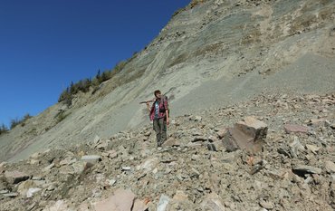 Ilya Bobrovsiy stands with a sledgehammer on his shoulder in a geological outcrop and gazes into the distance.