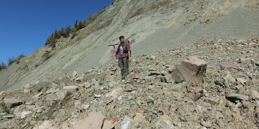 Ilya Bobrovsiy stands with a sledgehammer on his shoulder in a geological outcrop and gazes into the distance.