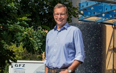 Portrait of a man in front of green trees and a stone column. GFZ Logo in the rear.