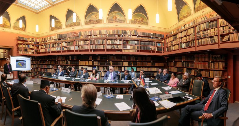 The reading room in the Historical Library: on the right, a woman stands and presents a lecture, in the room about 25 people sit at tables. Walls of books in the background.