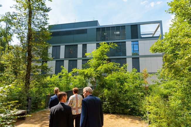 4 people walking towards a modern, light-coloured building surrounded by trees.