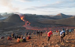 Viele Menschen sitzen am Rande eines flachen, gerade ausbrechenden Vulkans am Magmastrom