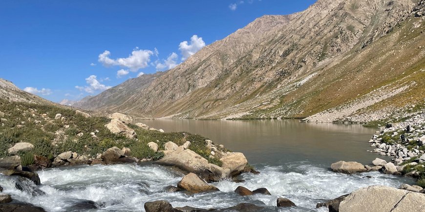 A lake, a foaming tributary in the foreground, bare mountain slopes on the sides.