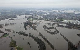 Image from the aircraft of a flat landscape that is flooded over a large area: fields, roads and parts of villages are under water.