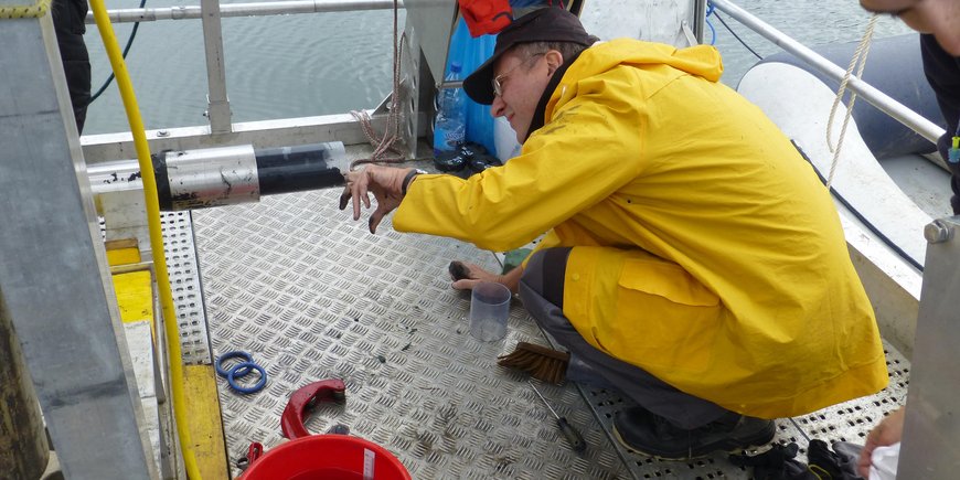 Achim Brauer in a yellow raincoat on a platform in the water looking at a sediment core freshly pulled out of the lake