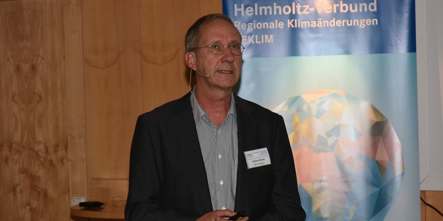 Achim Brauer stands in front of a REKLIM roll-up in the interior of a seminar room.