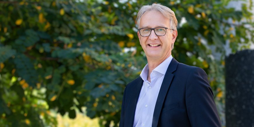 Dr Oliver Bens, man with grey-brown hair, light blue eyes and glasses, wearing a suit