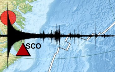 Die Seismologische Messung als schwarze Zitterkurve liegt über einer Landkarte von Grönland und angrenzendem Atlantischen Ozean.