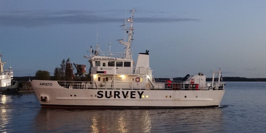 The photo shows the Finnish survey ship "Airisto" about 100 meters away from the viewer in the harbor basin of the Finnish town of Mäntyluoto. It has just cast off and is about to leave the harbor. The ship is facing the viewer with its port side. It is about 30 meters long and has the inscription "SURVEY" written on its side in capital letters. Above the bridge is the inscription www.meritaito.fi. This is the website of the shipping company of this ship.